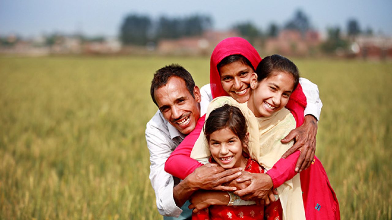 A smiling family of a mother and father and two children backdropped by a rural landscape